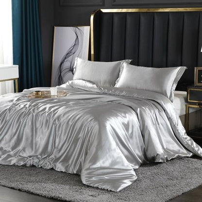 Luxuriöses silbernes Satin-Bettwäsche-Set auf modernem Bett mit Kopfteil und grauem Teppich.
