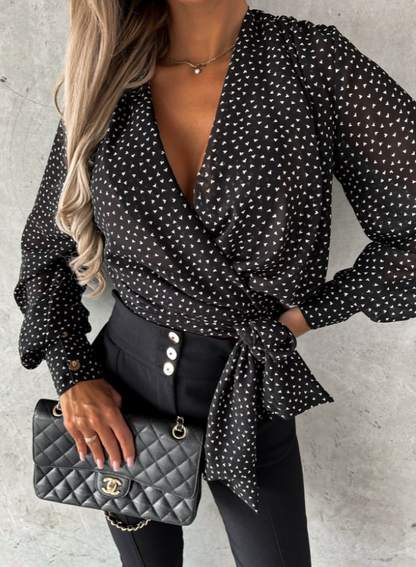 Frau in schwarzer Wickelbluse mit weißen Punkten, schwarze Hose, Chanel-Tasche, modisch, elegant.