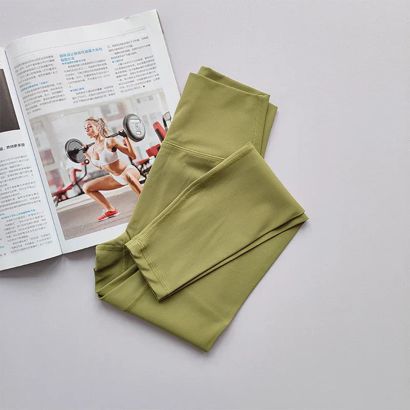 Olivgrüne Sportleggings aus Stretchmaterial neben Fitnessmagazin auf grauem Hintergrund.