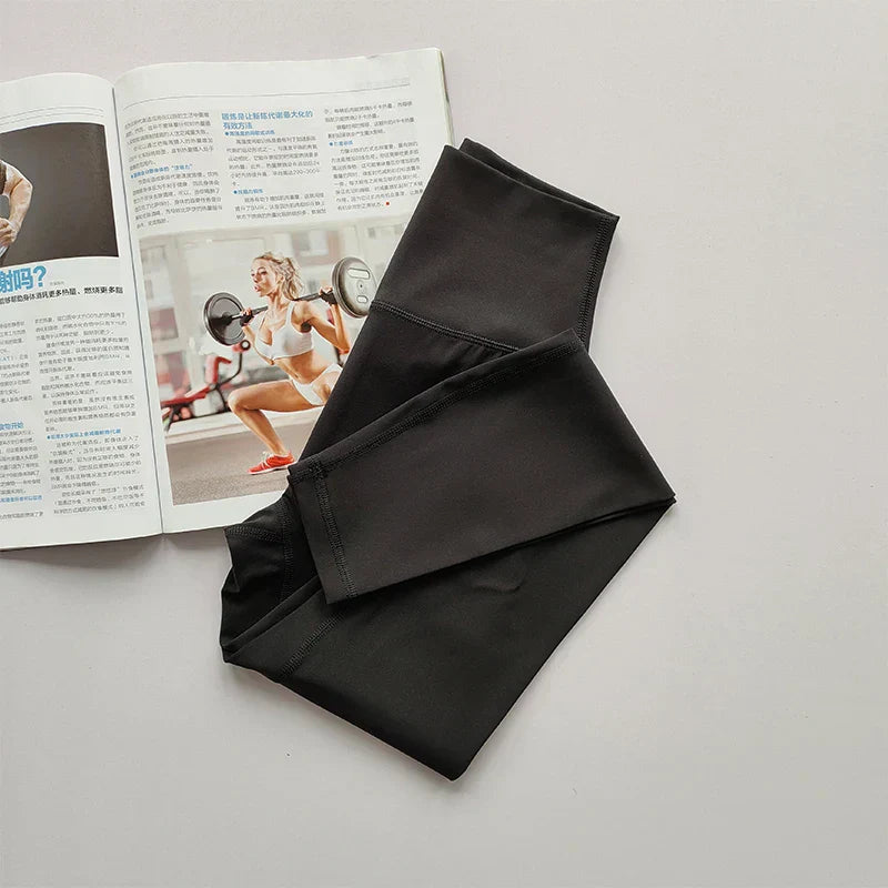 Schwarze Sportleggings aus Stretchmaterial neben Fitnessmagazin auf grauem Hintergrund.