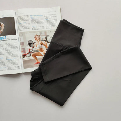 Schwarze Sportleggings aus Stretchmaterial neben Fitnessmagazin auf grauem Hintergrund.