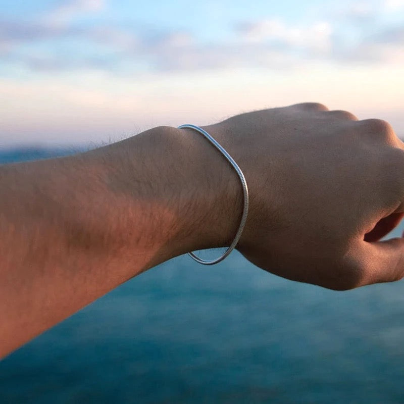 Silberarmband am Handgelenk vor Meereshorizont, minimalistisches Schmuckdesign.