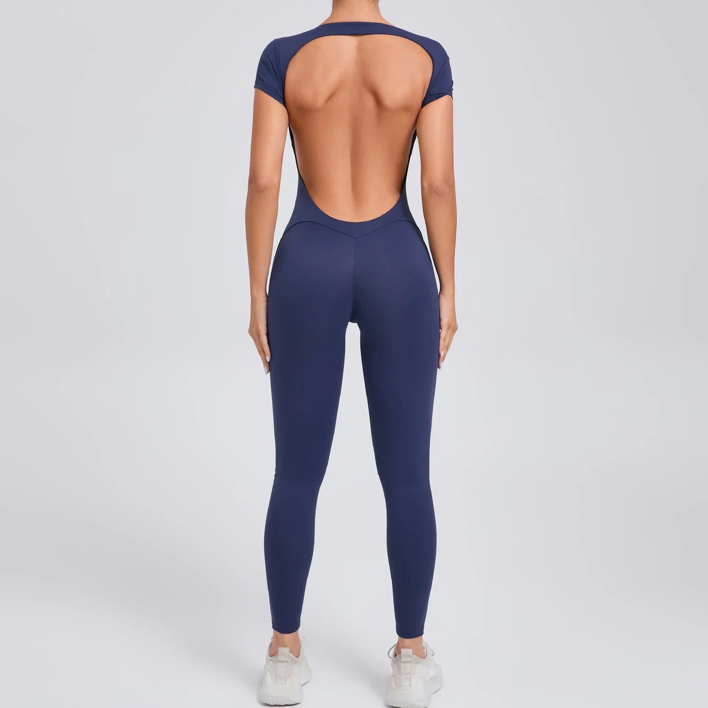 Frau in dunkelblauem, rückenfreiem Jumpsuit, Sportbekleidung, Ganzkörperansicht von hinten.