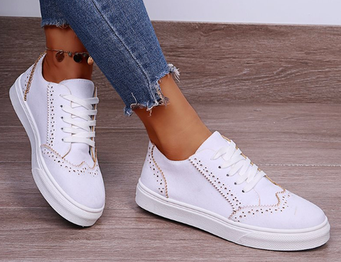 Weiße Damen-Sneaker mit Lochmuster, Jeans, Holzfußboden, modisch, bequem.