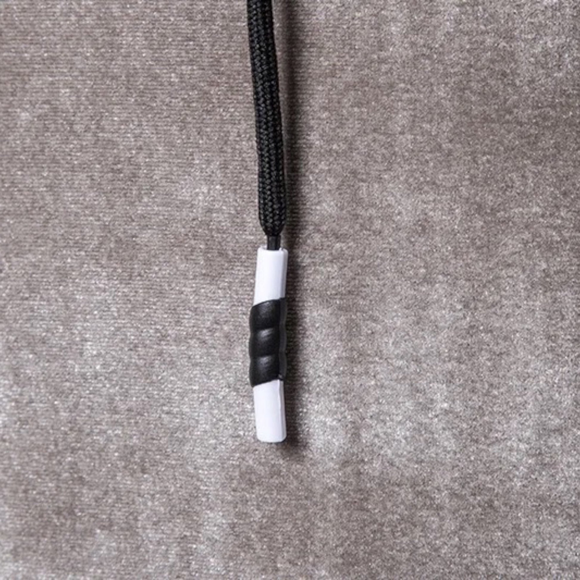 Schwarze und weiße Kordelstopper auf grauem Stoffhintergrund, Textilzubehör.