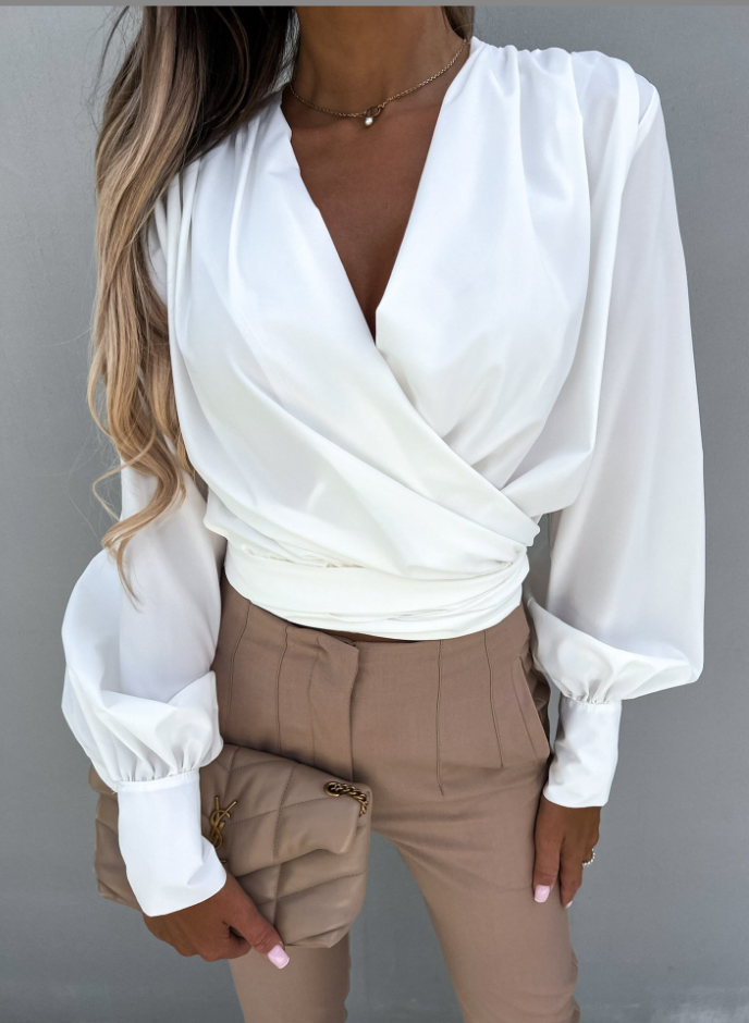Frau in weißer Wickelbluse und beiger Hose hält beige Clutch, elegante Mode.