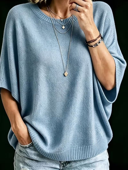 Närbild på blå stickad topp med batwing-ärmar och rund hals, med handen i jeansfickan. 12