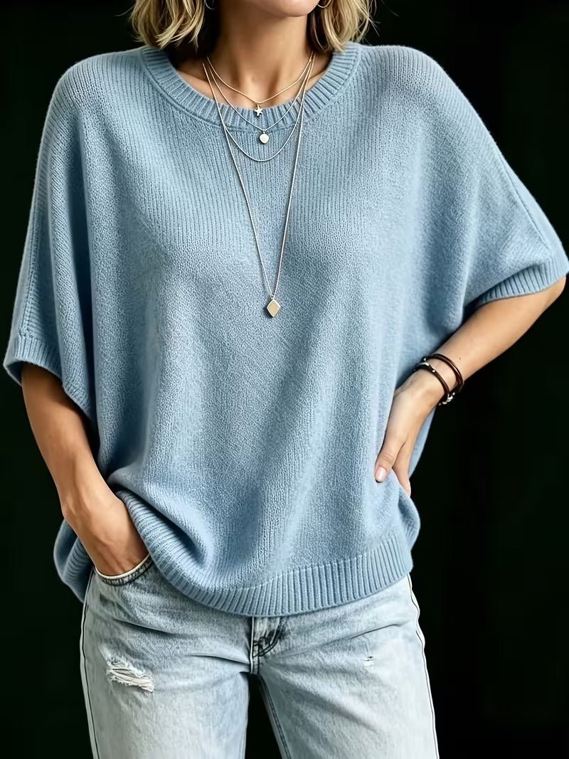 Blå stickad topp framifrån på modell med ena handen i jeansfickan och den andra på höften. 15