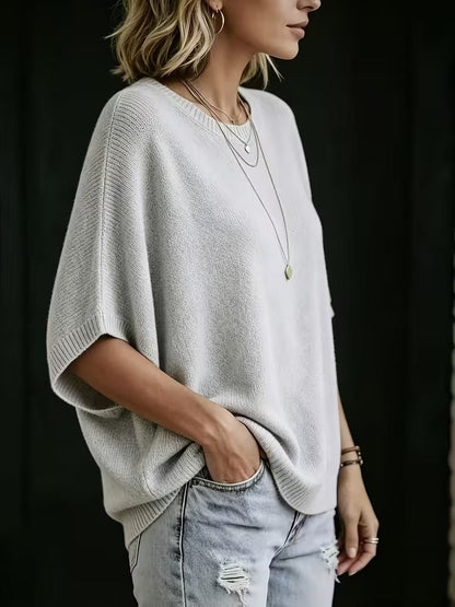 Ljusgrå stickad topp i sidovy på modell med handen i jeansfickan, de vida batwing-ärmarna syns tydligt. 2