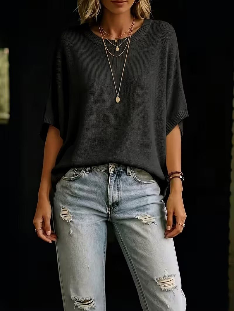 Svart stickad topp med korta batwing-ärmar sedd framifrån på modell, stylad med slitna ljusa jeans och långa halsband. 27