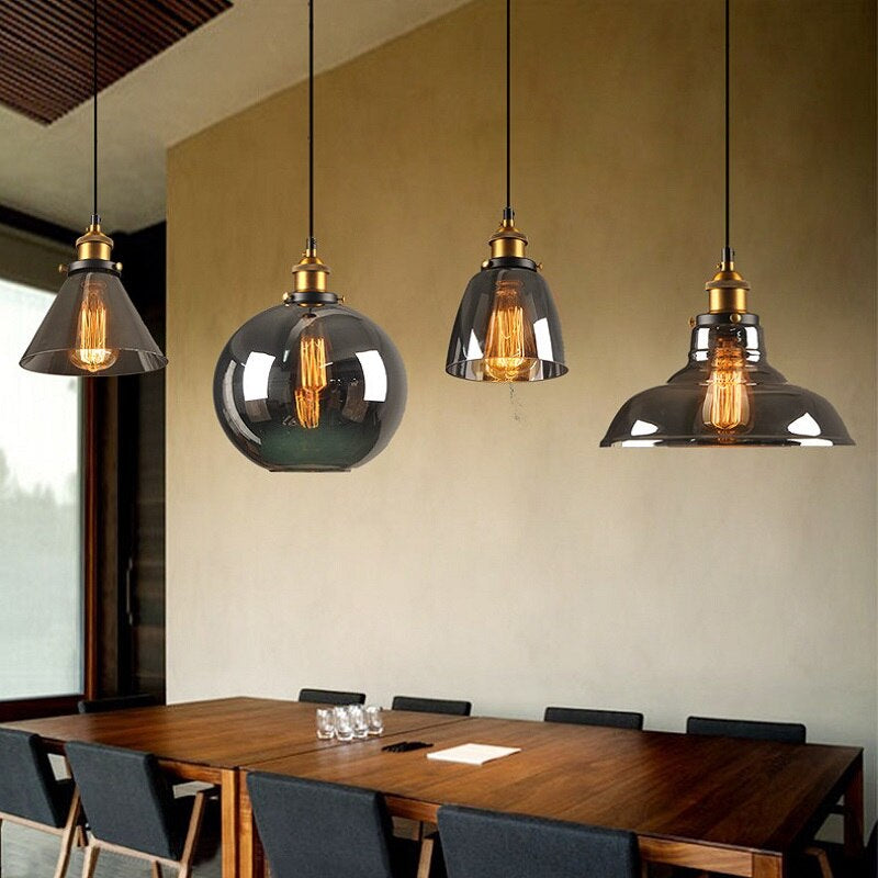 Vier moderne Pendelleuchten über Esstisch, Glas und Metall, industrielles Design, warmes Licht.