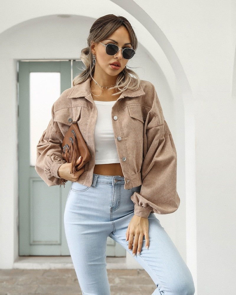 Frau in beiger Cordjacke und blauer Jeans, modisch, lässig, Sonnenbrille, weißes Top.
