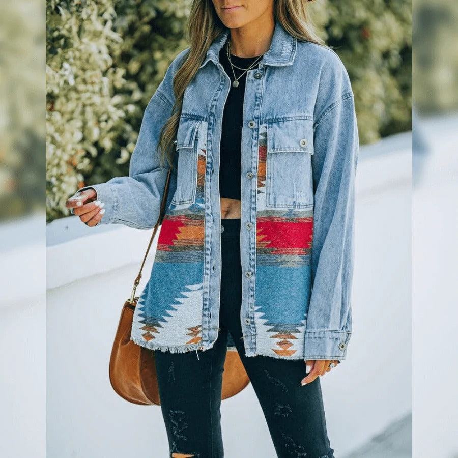 Frau in blauer Jeansjacke mit buntem Aztekenmuster, schwarze Hose, braune Tasche.