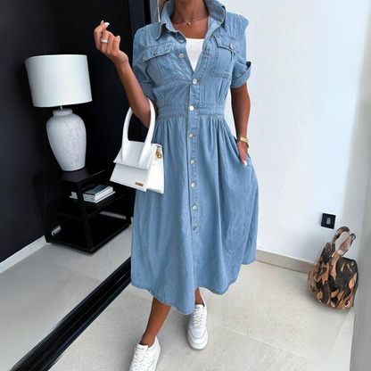 Frau in blauem Jeanskleid mit weißer Handtasche und Sneakers in modernem Raum.