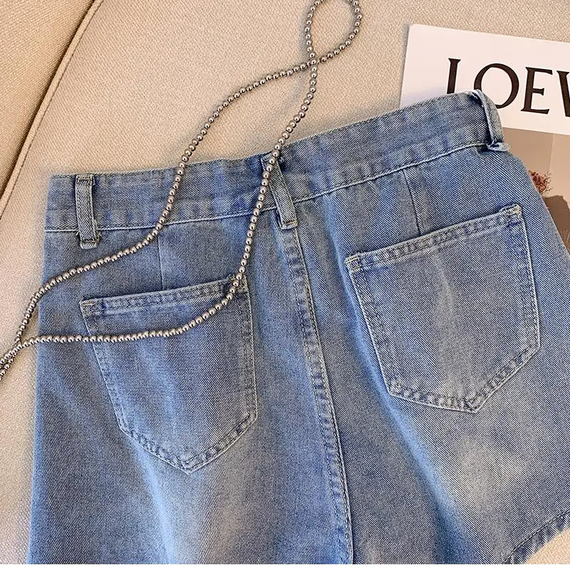 Hellblaue Jeansrock mit Taschen und Kettengürtel auf beigem Sofa, modisch, Damenbekleidung.
