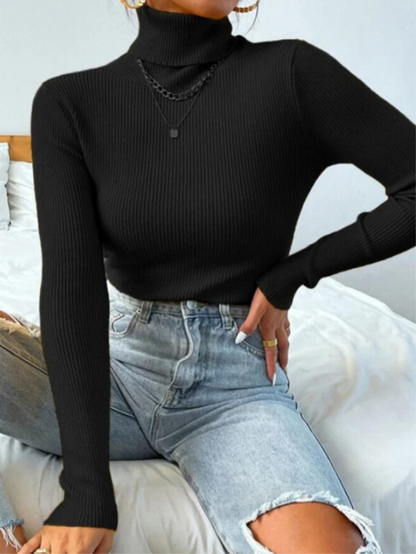 Frau in schwarzem Rollkragenpullover und blauer Jeans auf Bett sitzend, modisch, elegant.