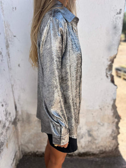 Frau in silberner Metallic-Bluse, seitlich, vor weißer Wand, modisch, elegant, glänzend.