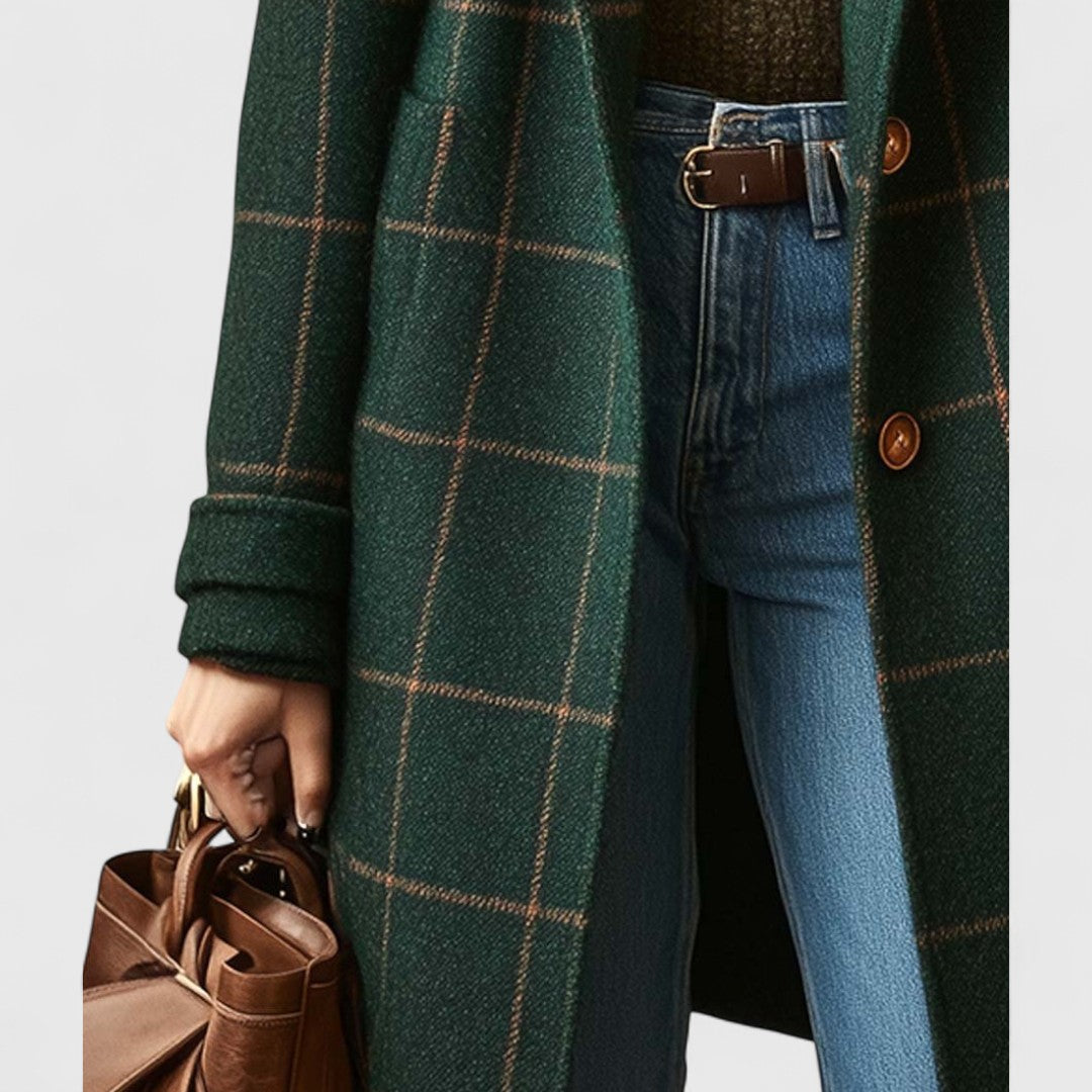 Närbild på kappans nedre del med fickor, uppvikt ärm, knappar och jeans, med en brun läderväska i handen. 4