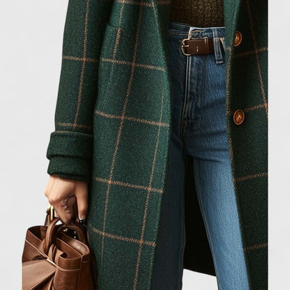 Närbild på kappans nedre del med fickor, uppvikt ärm, knappar och jeans, med en brun läderväska i handen. 4