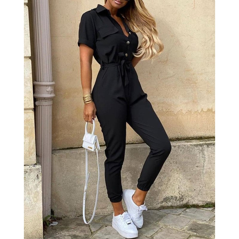 Frau in schwarzem Jumpsuit mit Gürtel, kurzen Ärmeln, weißen Sneakers, modisch, elegant.