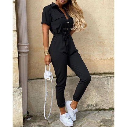 Frau in schwarzem Jumpsuit mit Gürtel, kurzen Ärmeln, weißen Sneakers, modisch, elegant.