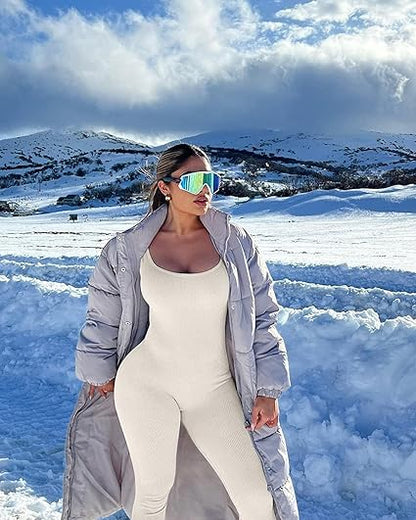 Frau in weißem Jumpsuit und grauem Mantel im Schnee, trägt bunte Sonnenbrille.
