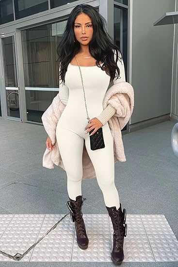 Frau in weißem Langarm-Jumpsuit, schwarze Stiefel, rosa Jacke, moderne Architektur im Hintergrund.