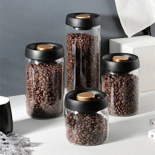 Vier Glasbehälter mit schwarzen Deckeln, gefüllt mit Kaffeebohnen, auf grauem Hintergrund.