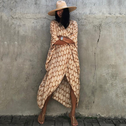 Frau in beige-gemustertem Kaftan und Strohhut vor Betonwand, Sommermode, lässiger Stil.