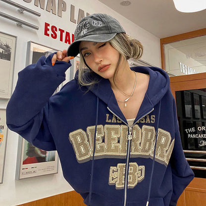 Frau in blauer Kapuzenjacke mit "BEERBR" Aufdruck und grauer Kappe, lässiger Streetwear-Look.