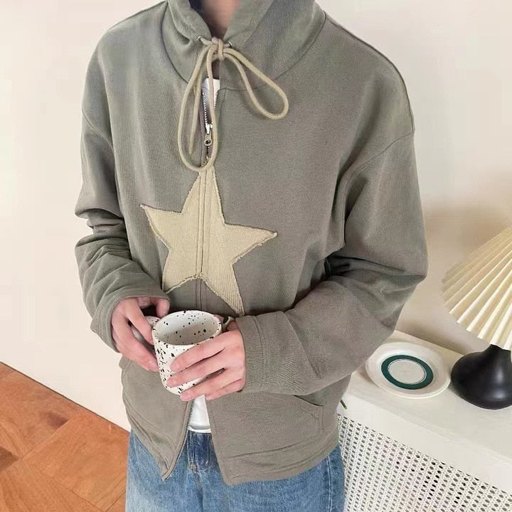 Person in olivgrüner Kapuzenjacke mit Sternmotiv hält Tasse, lässige Mode, gemütlicher Stil.