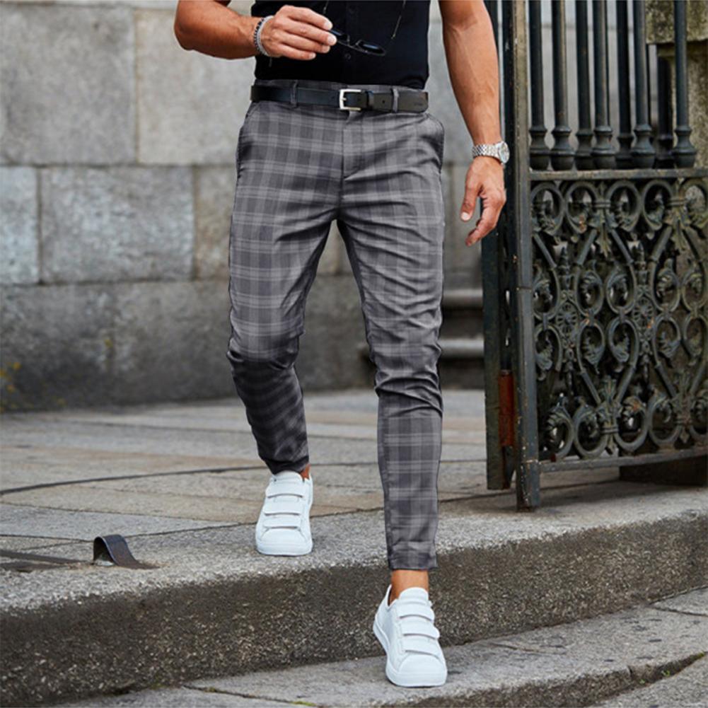 Mann in grauer karierter Hose, weißem Sneaker, schwarzem T-Shirt, modisch, urbaner Stil.