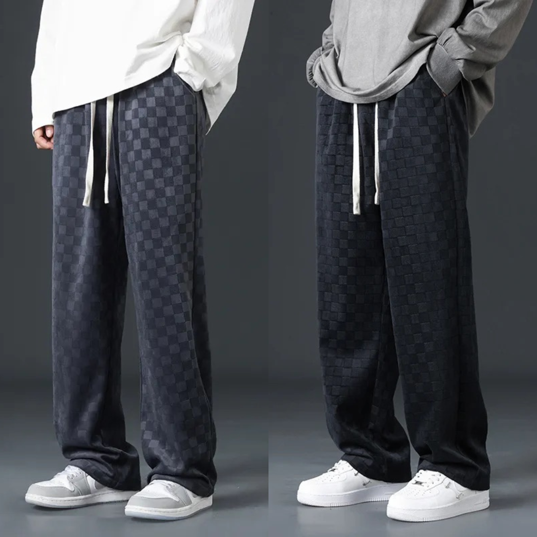 Zwei Herren in karierten, dunkelgrauen Jogginghosen und Sneakers vor grauem Hintergrund.
