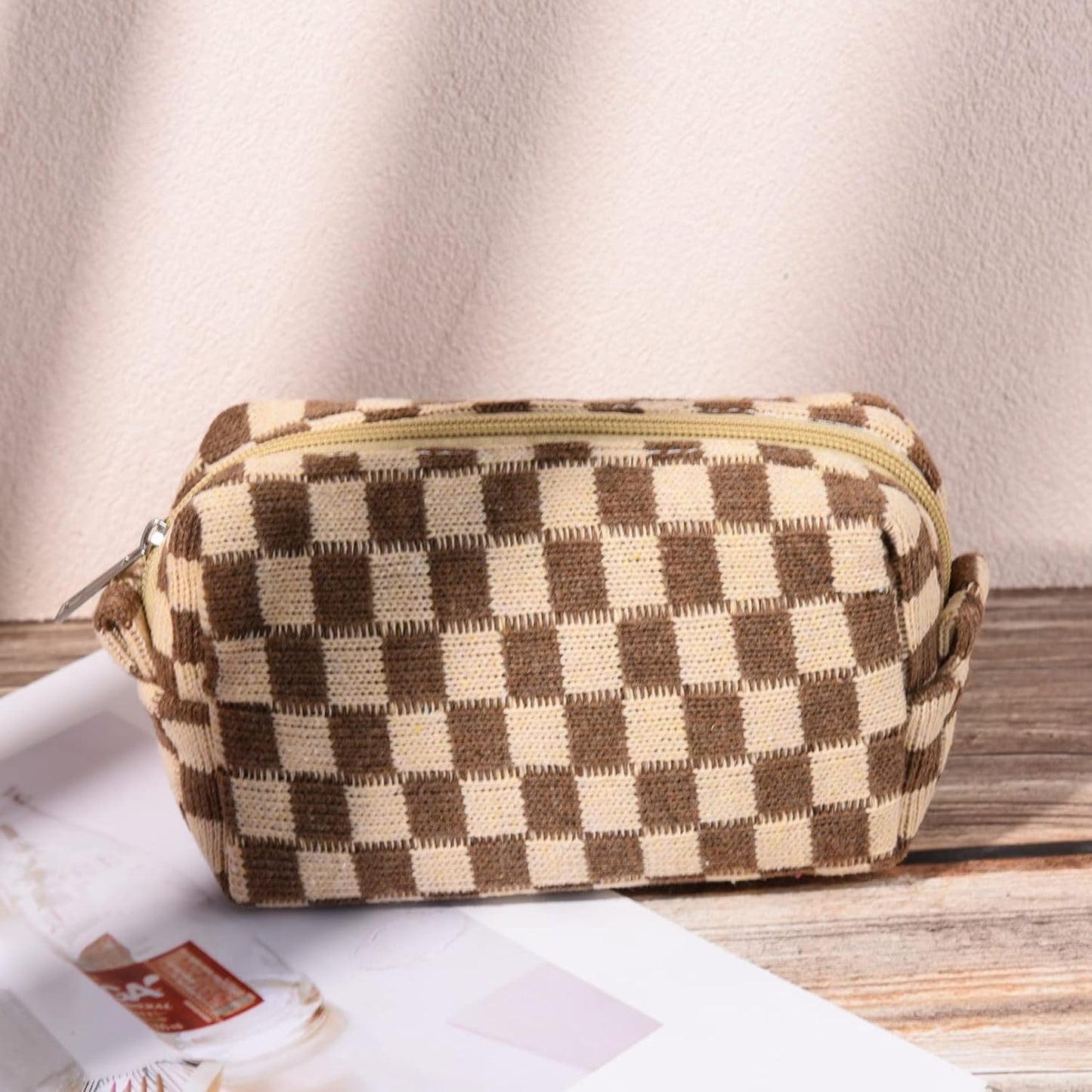 Braune karierte Kosmetiktasche aus Stoff mit Reißverschluss auf Holztisch, stilvoll und praktisch.