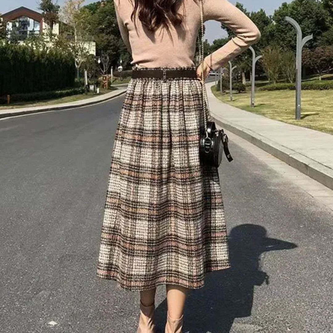 Frau in karierter Wollrock, beige Pullover, Straße, Herbstmode, eleganter Stil.
