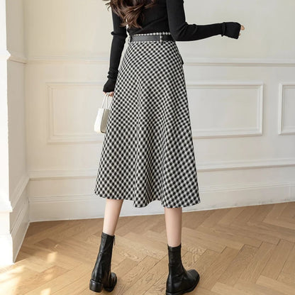Frau in schwarz-weißem Karorock, schwarzem Pullover, Stiefeletten, weiße Handtasche.