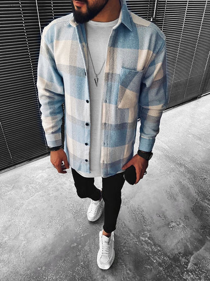 Mann in kariertem Hemd, weißem T-Shirt, schwarzer Hose und weißen Sneakers, modern gekleidet.