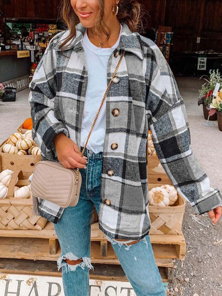 Frau in kariertem Oversize-Hemd, Jeans, beige Tasche, Herbstmarkt, Kürbisse im Hintergrund.