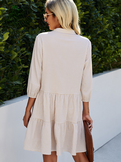 Frau in kariertem Sommerkleid, blond, Sonnenbrille, draußen, grüne Hecke im Hintergrund.