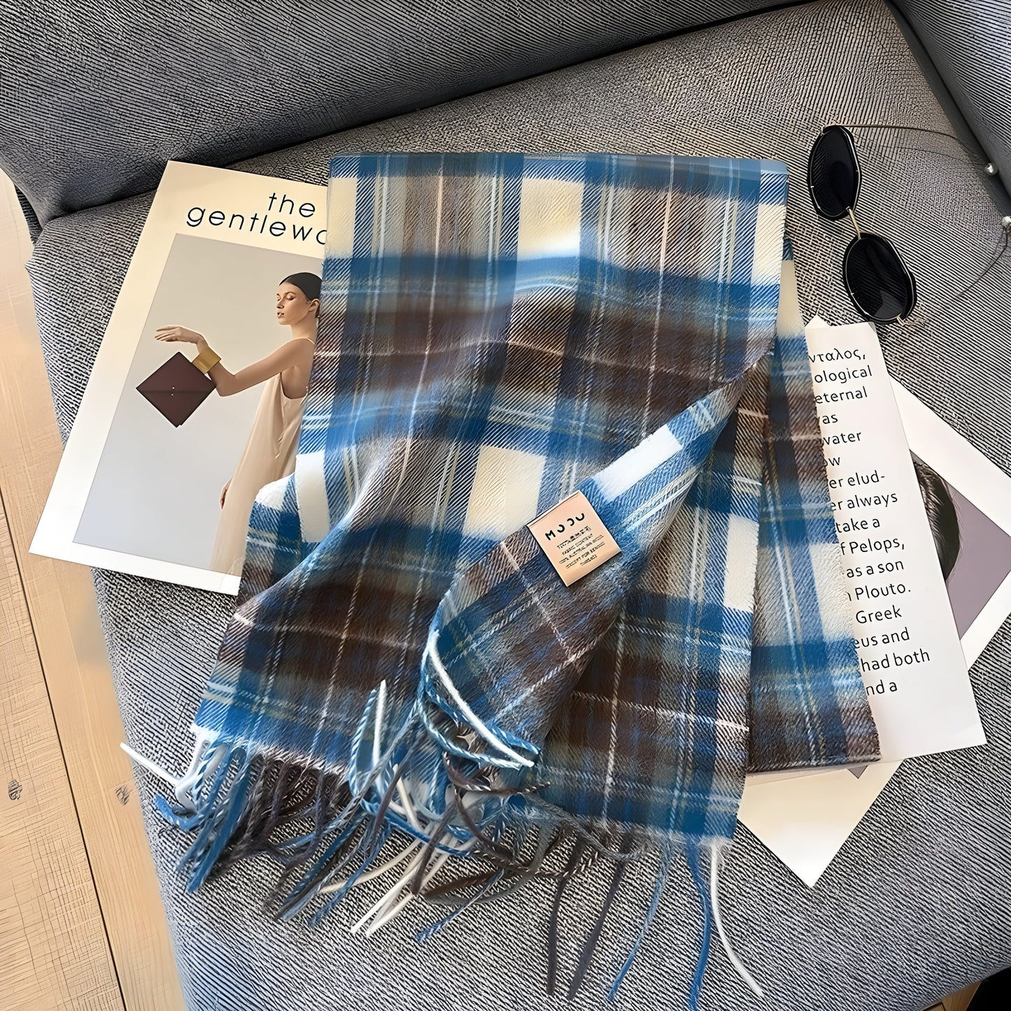 Blau-weiß karierter Wollschal mit Fransen auf grauem Sofa, modisches Accessoire.