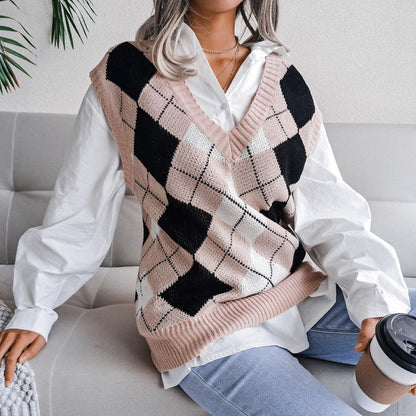 Frau in kariertem Strickpullover, weißer Bluse, Jeans, hält Kaffeebecher, sitzt auf Sofa.