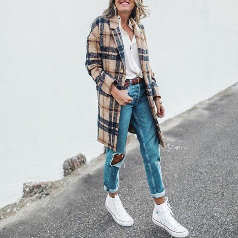 Frau in kariertem Mantel, weiße Bluse, zerrissene Jeans, weiße Sneaker, lässiger Streetstyle.
