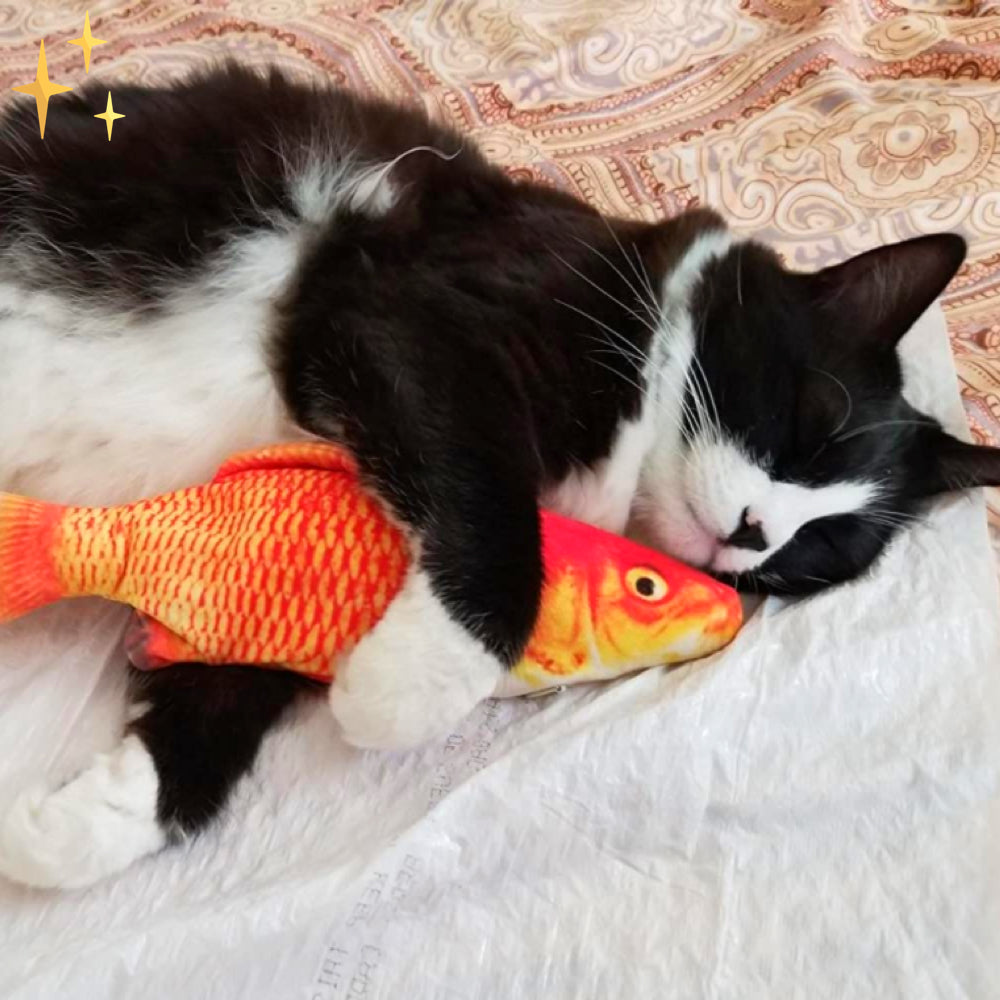 Schwarz-weiße Katze kuschelt mit orangefarbenem Fischspielzeug auf gemustertem Bettbezug.