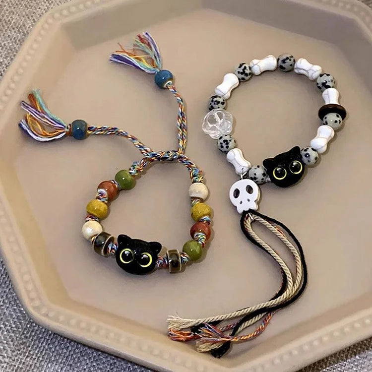 Zwei handgefertigte Armbänder mit Katzen- und Totenkopf-Perlen auf einem Teller.