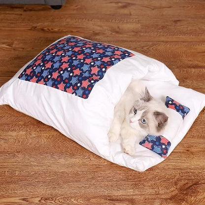 Weiße Katzendecke mit blau-rotem Sternenmuster, Katze kuschelt darin, auf Holzboden.