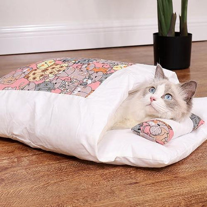 Katze in weißem Kissenbett mit buntem Muster, Holzfußboden, Zimmerpflanze im Hintergrund.