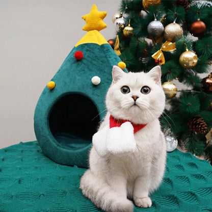 Weißer Katze mit rotem Schal vor grünem Weihnachtsbaum-Katzenbett, Weihnachtsdekoration.