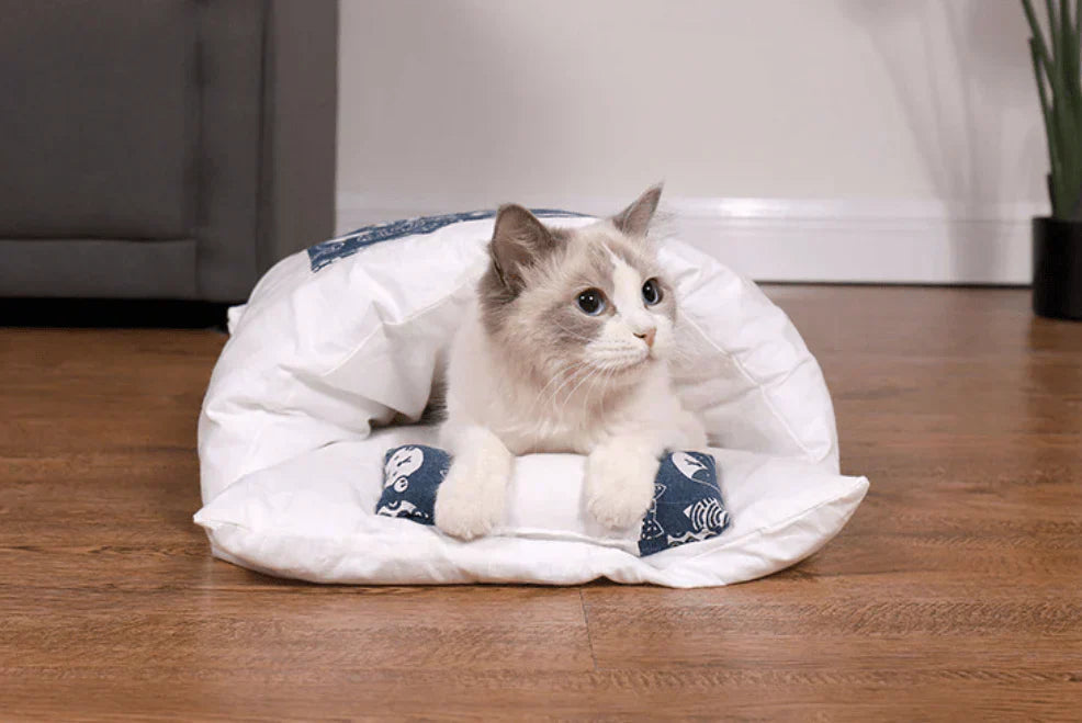 Katzenbett aus weißem Stoff mit blauem Muster, gemütlich, für Haustiere, auf Holzboden.