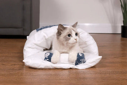 Katzenbett aus weißem Stoff mit blauem Muster, gemütlich, für Haustiere, auf Holzboden.