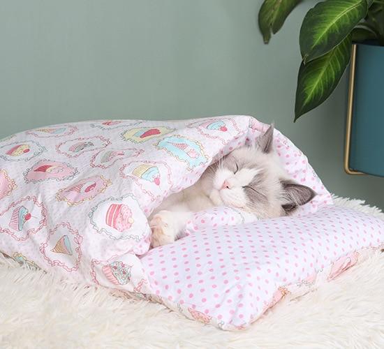 Schlafende Katze in rosa Bettwäsche mit Herz- und Punktmuster, gemütlich auf weißem Teppich.